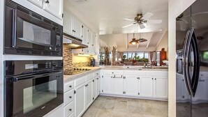 A modern kitchen with white cabinets, a black oven, a black refrigerator, and a ceiling fan. - Spacious Executive Retreat in Paradise + 3 mins from Turtle Beach! (Kailua-Kona)
