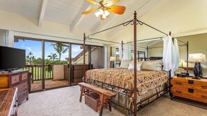 A spacious bedroom with a four-poster bed, a ceiling fan, a television, and a balcony with a view of palm trees. - Spacious Executive Retreat in Paradise + 3 mins from Turtle Beach! (Kailua-Kona)