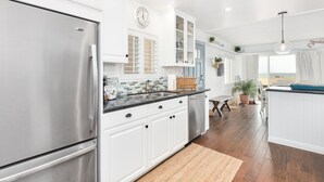 Una cocina moderna con armarios blancos, un refrigerador de acero inoxidable, un salpicadero de azulejos y una mesa de comedor de madera con sillas.