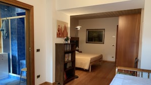 Een slaapkamer met een houten vloer, een bed, een nachtkastje, een boekenkast en een raam met uitzicht op een blauw betegeld gebied.