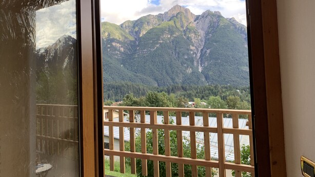 Uitzicht vanaf een balkon met houten balustrade, over een vallei met bergen en een rivier.