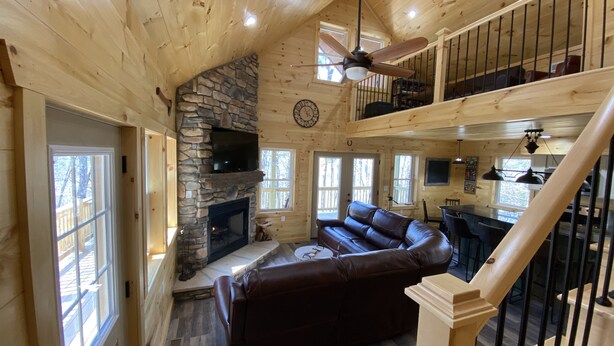 L’intérieur d’un chalet en bois, avec une cheminée en pierre, un canapé en cuir et un coin repas.