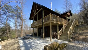 Une cabane en bois dotée d’un balcon, d’une terrasse couverte et d’un escalier en pierre.