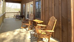 Une terrasse en bois avec des fauteuils à bascule et une table, un ventilateur de plafond et de grandes fenêtres.