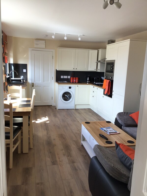 A compact living space with a kitchen, a washing machine, a dining area, and a seating area with a sofa and a coffee table.