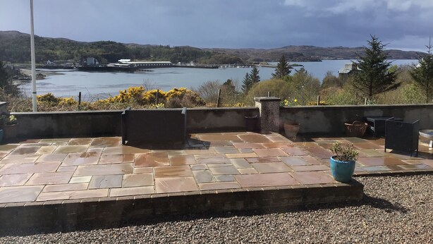 A patio with stone tiles, a flag, and a view of a lake and hills. - Studio (Lochinver)