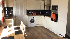A compact kitchen with a washing machine, a microwave, and a dining area with a table and chairs. - Studio (Lochinver)