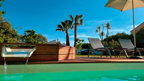 A poolside area with lounge chairs, a water feature, and palm trees. - Domaine Le Courti (Le Barcares)
