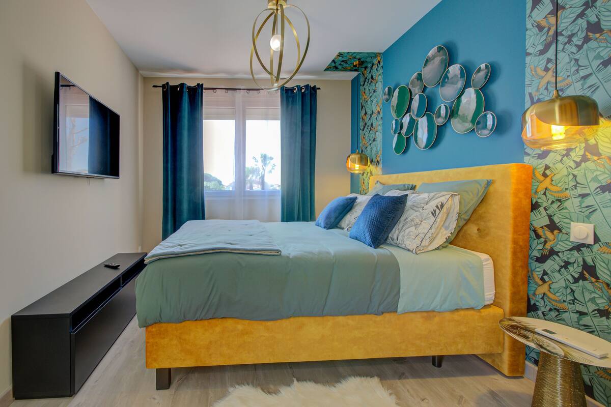 A bedroom with a bed, a flat-screen TV, a desk, and a window with curtains.