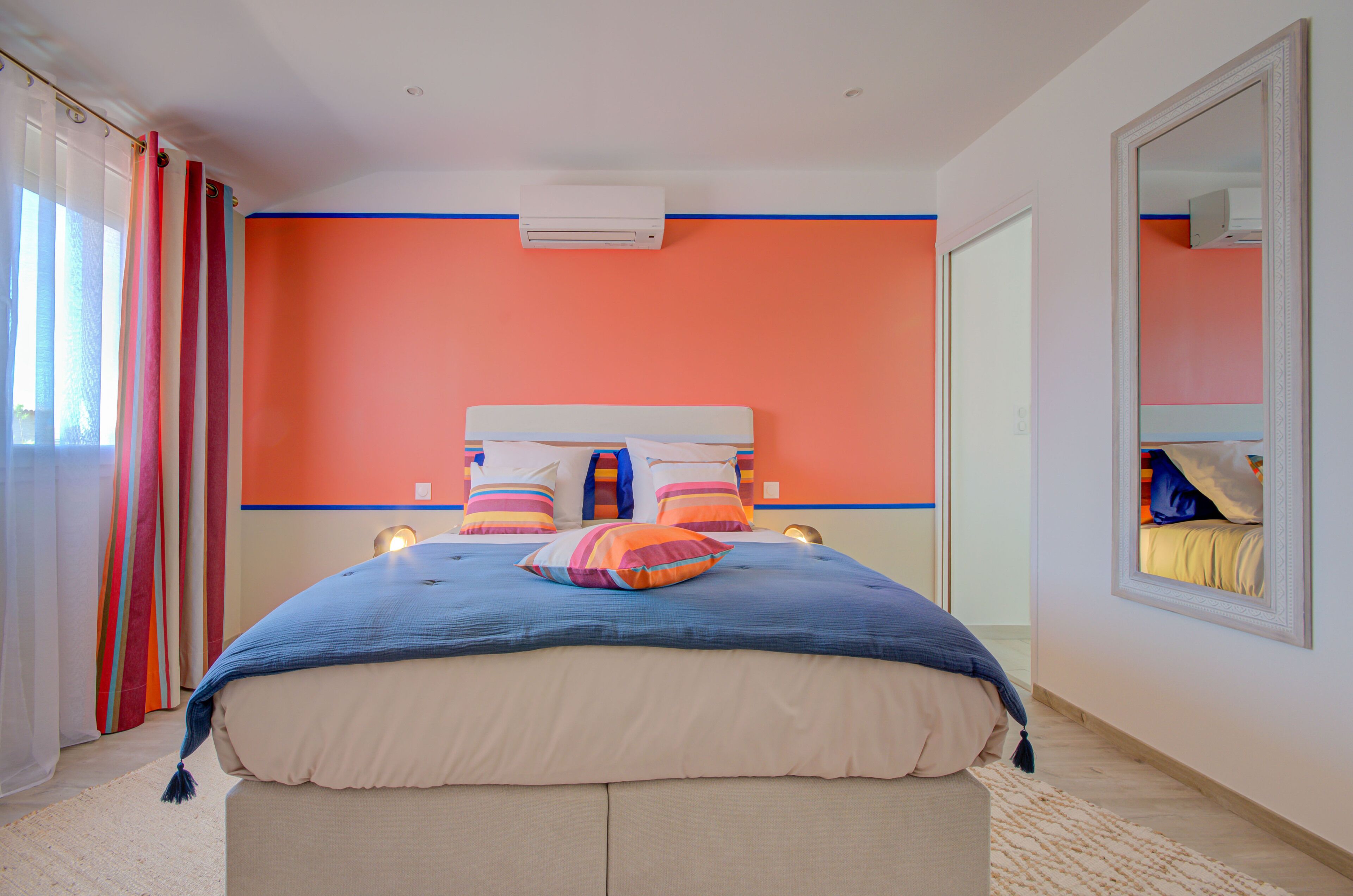 A bedroom with a large bed, a headboard, an air conditioner, and a mirror on the wall.