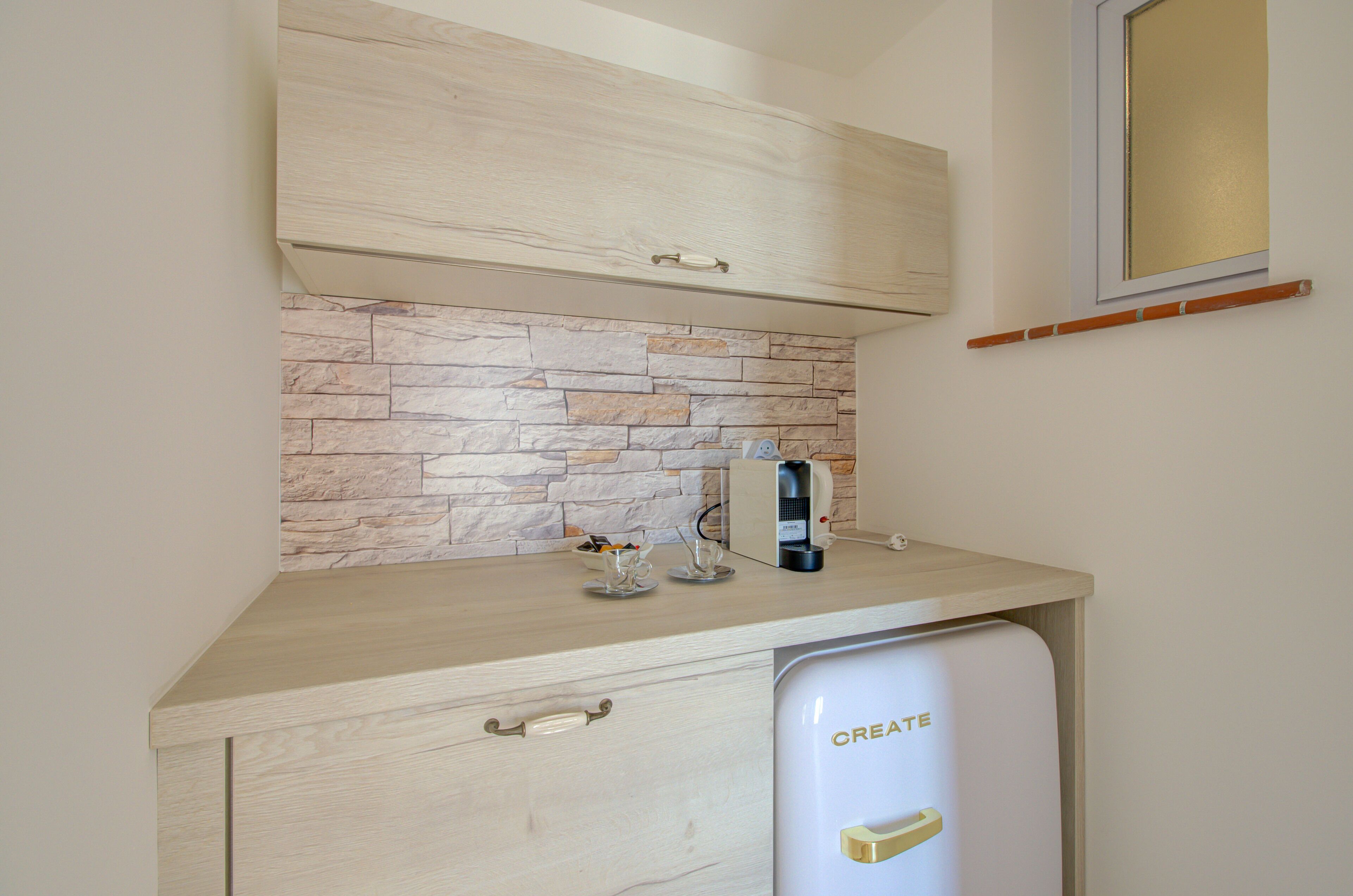 A kitchen with a stone backsplash, a coffee maker, and a refrigerator with a handle labeled "CREATE".