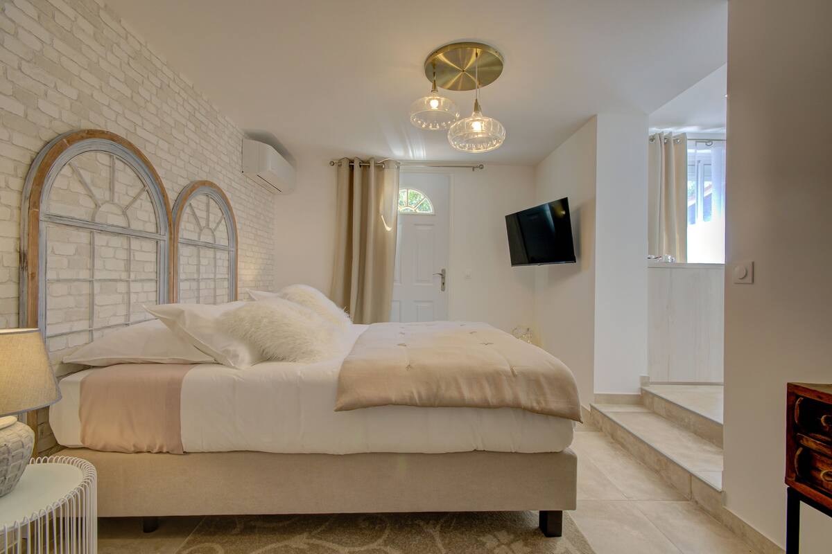 A bedroom with a large bed, a TV mounted on the wall, and a staircase leading to another room.
