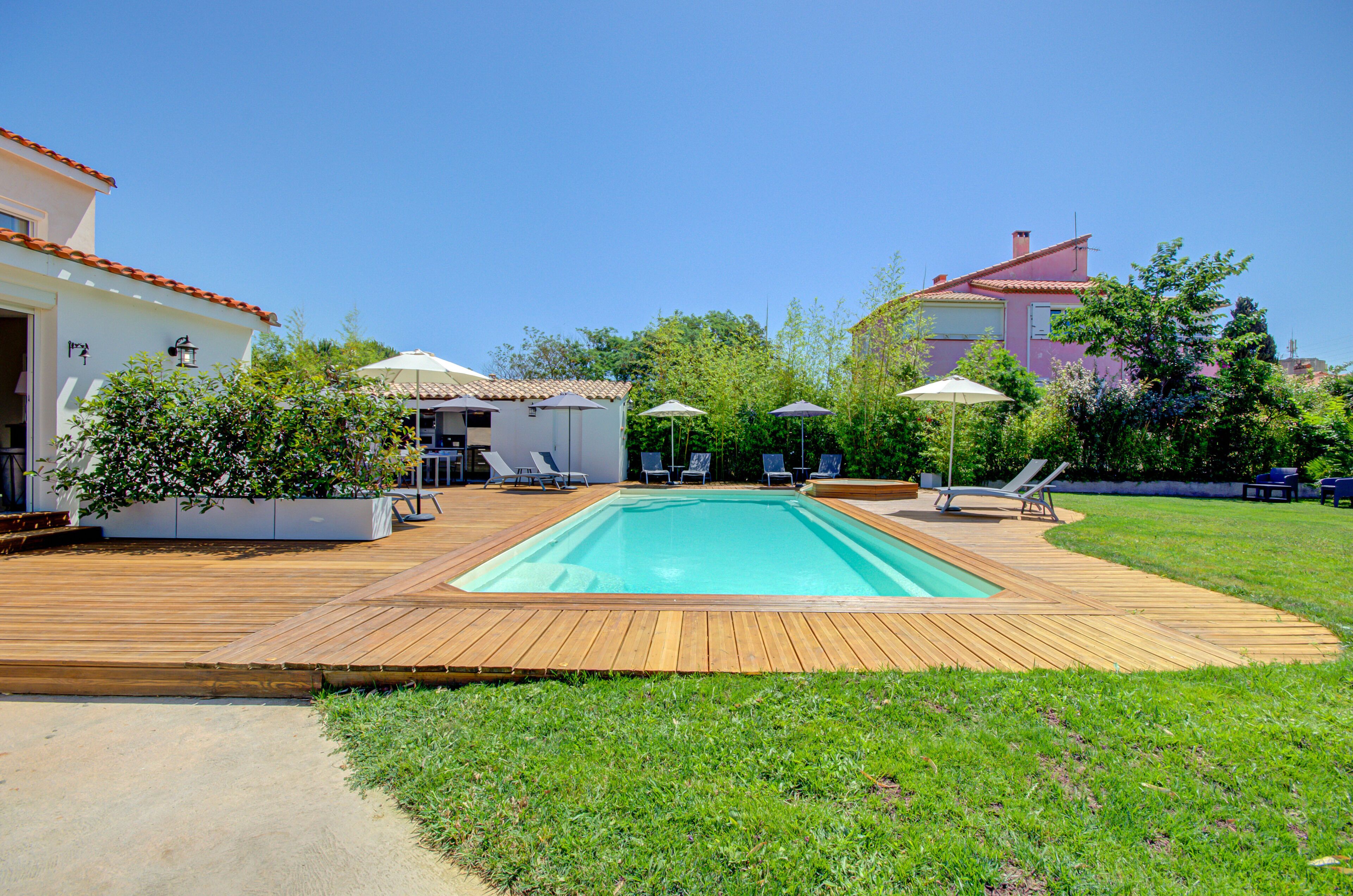 A rectangular swimming pool with a wooden deck, surrounded by grass and trees.
