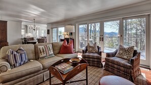A spacious living room with a large window, a sofa, a chair, and a coffee table. - Charming Cashiers Cottage with View of Chimney Rock Adjoining High Hampton (Cashiers)