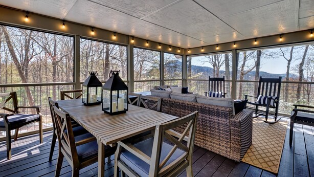 A covered outdoor seating area with a wooden table and chairs, a wicker sofa, and string lights. - Charming Cashiers Cottage with View of Chimney Rock Adjoining High Hampton (Cashiers)