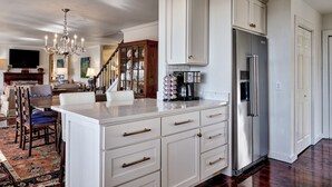 A spacious kitchen with white cabinetry, a stainless steel refrigerator, and a dining area with a wooden table and chairs. - Charming Cashiers Cottage with View of Chimney Rock Adjoining High Hampton (Cashiers)