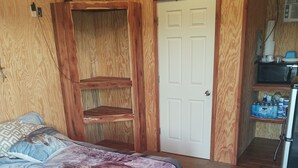 A bedroom with a bed, wooden walls, a white door, and a kitchenette area. - Little Cabin at the DonkeyRanch (Lawton)