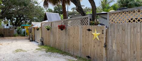 Une clôture en bois ornée d’une étoile, un chemin de gravier et un petit espace jardin avec des plantes en pot.