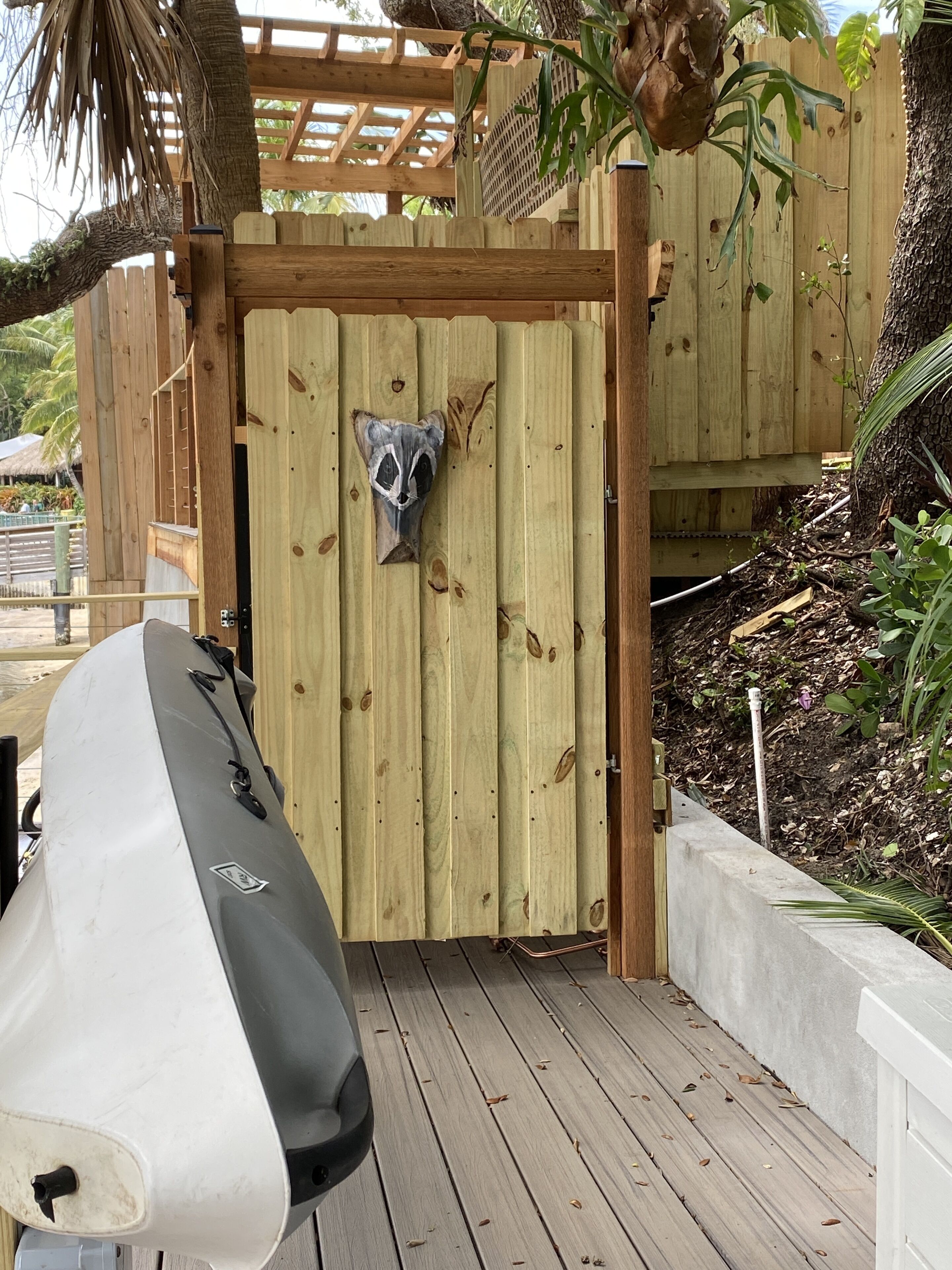 A wooden gate with a raccoon mask, a covered wooden deck, and a white boat.