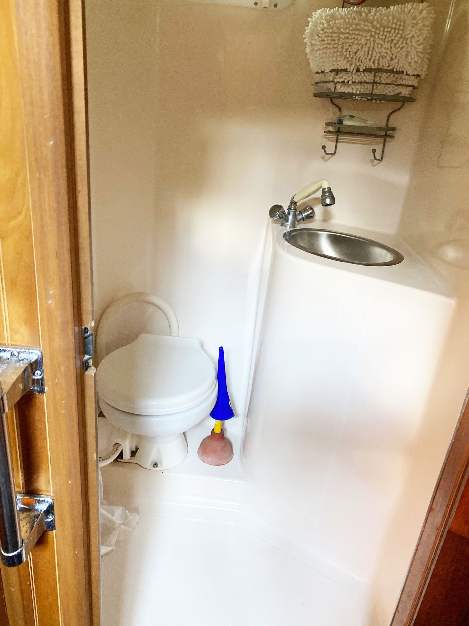 Een kleine, praktische badkamer met een toilet, wastafel en een blauwe ontstoppingszuiger.