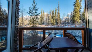 A balcony with a table and chairs, overlooking a mountainous landscape with trees and a clear sky. - Lux Blackstone Mountain Suite with Amazing Views (Canmore)