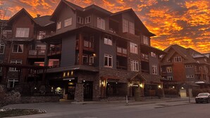 A multi-story building with a stone facade and multiple balconies, under a sunset sky. - Lux Blackstone Mountain Suite with Amazing Views (Canmore)