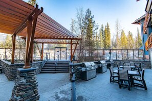 Eine Terrasse im Freien mit Steinsäulen, Holzbanken und Grillanlagen.