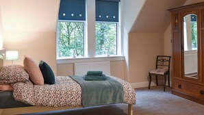 Une chambre à coucher comprenant un lit, une chaise, une armoire et une fenêtre donnant sur des arbres.