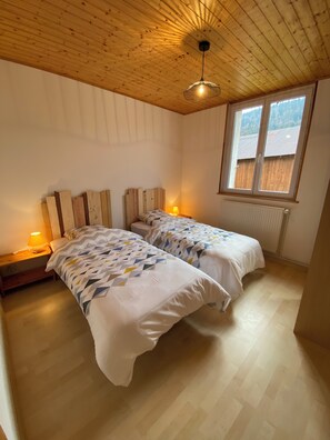 Two single beds with patterned duvets, a window with an outside view, and a radiator below.