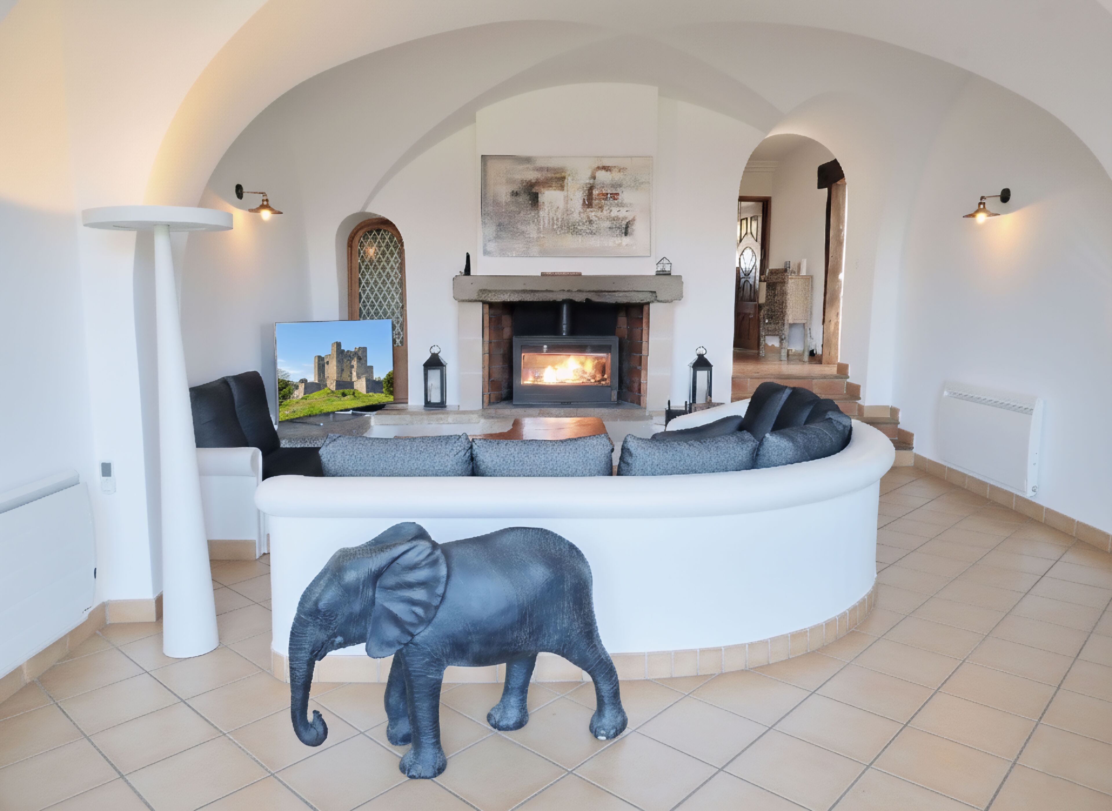 Un salon moderne avec un canapé blanc aux lignes courbes, une cheminée et une grande statue d’éléphant.