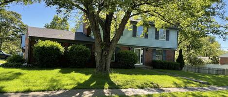 A two-story house with a large tree in front, a well-maintained lawn, and a wooden fence.