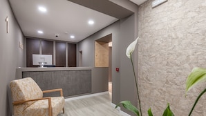 A reception area with a reception desk, a chair, a plant, and a stone wall. - Zarco B&B - Bed and Breakfast (Funchal)