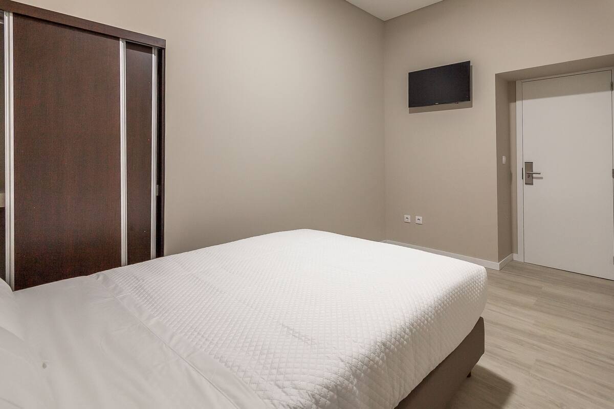 A bedroom with a bed, a wardrobe, a door, and a wall-mounted TV.