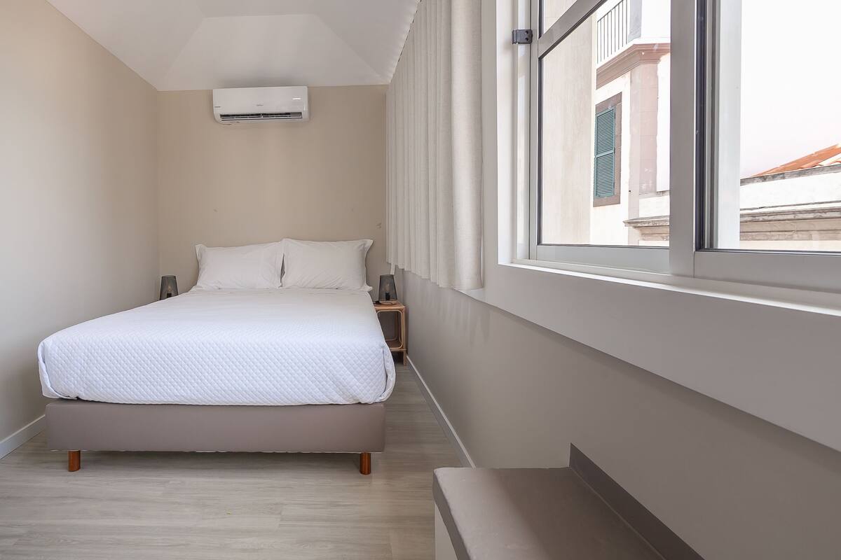 A neatly arranged bedroom with a bed, bedside tables, and a window with curtains.
