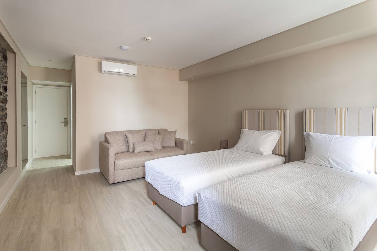 A bedroom with a bed, a sofa, and a door leading to another room.