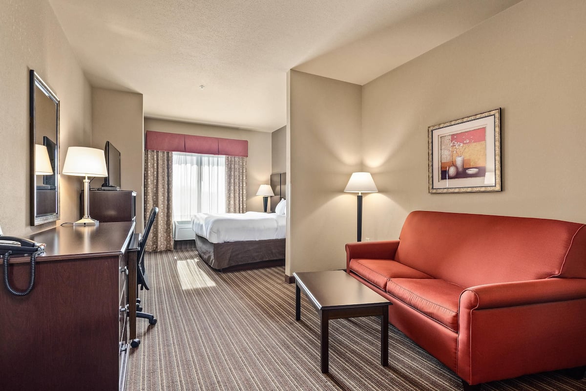 A hotel room with a bed, a desk with a telephone, a red sofa, a small table, and a framed picture on the wall.