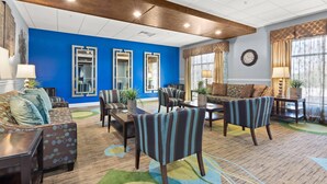 A hotel lobby with a blue accent wall, wooden ceiling beams, and a variety of seating options including sofas and chairs. - Portland Inn & Suites (Portland)