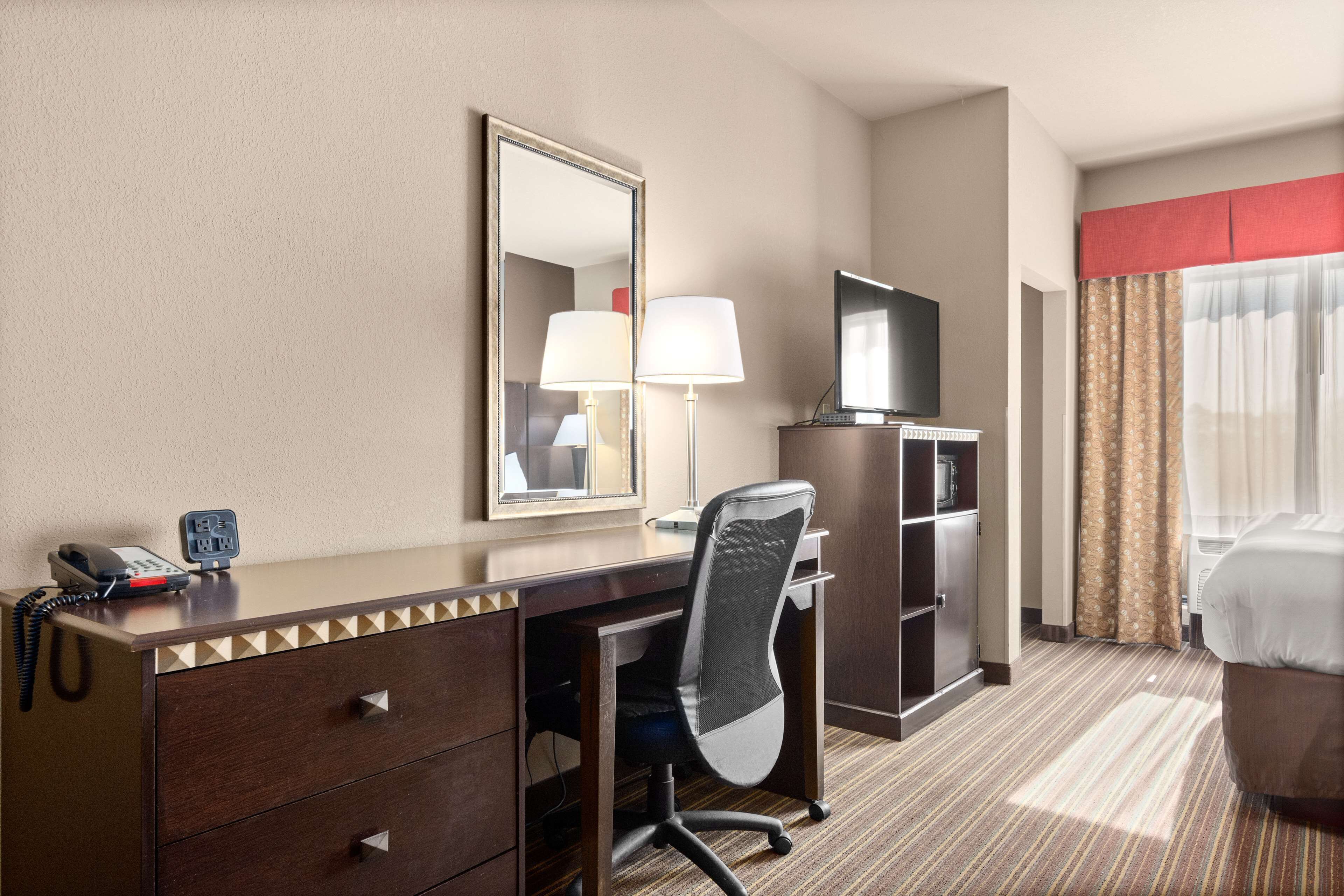 A hotel room with a desk, chair, dresser, TV, and a bed. - Portland Inn & Suites (Portland)