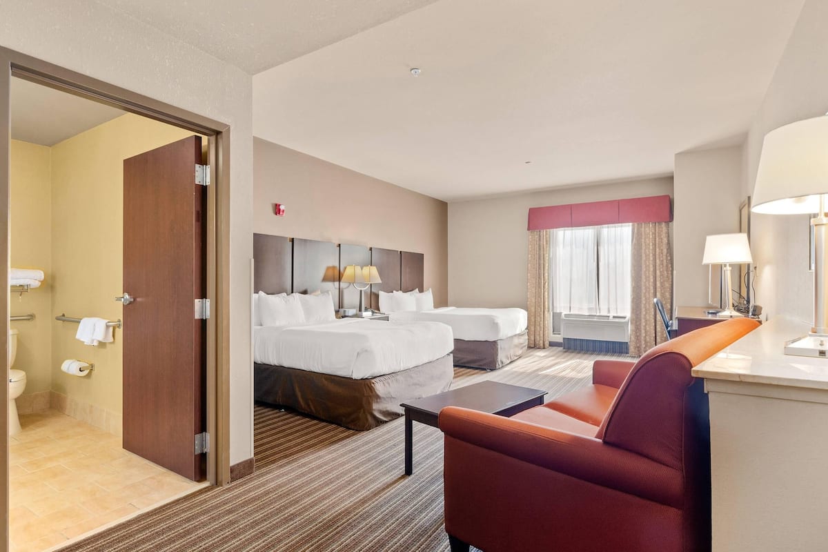 A hotel room with two beds, a desk, a chair, a bathroom, and a window with curtains.
