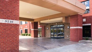 A building entrance with a brick facade, a numbered sign, and a covered walkway leading to a glass door entrance. - Portland Inn & Suites (Portland)