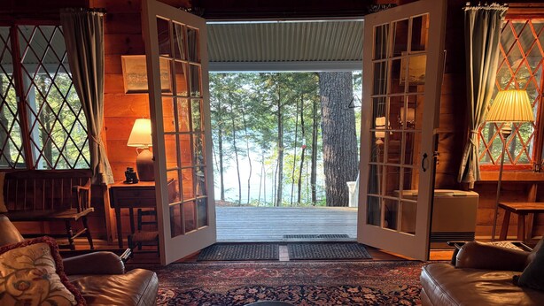 A cozy room with leather sofas, a patterned rug, and a large window with a view of trees.