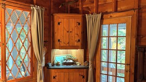 A wooden cabin interior with a wooden bench, a cabinet with a small table, and a window with curtains.