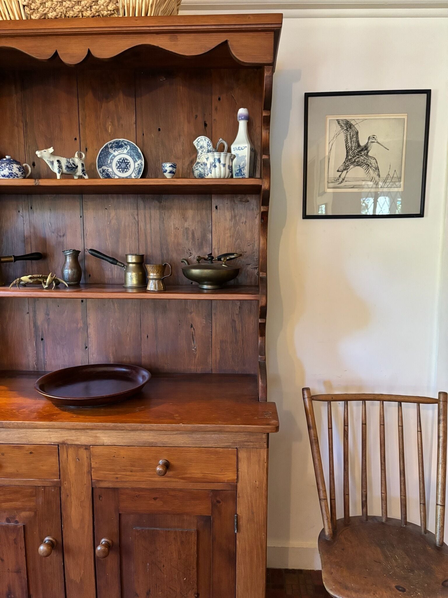 A wooden cabinet with shelves holding various kitchenware and a framed artwork on the wall.
