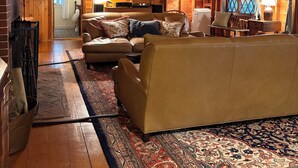 A cozy log cabin interior with a high ceiling, a fireplace, a sofa, and a patterned rug.