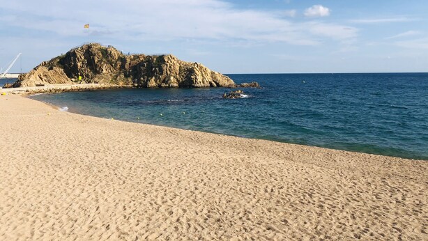 En sandstrand med en klippeformation i baggrunden og roligt hav.