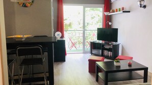 En stue med fjernsyn, et lille bord, en sofa og et spiseområde med stole og bord.