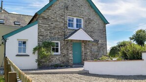 Une maison en pierre avec une porte verte et des boiseries blanches, un petit jardin et une allée gravillonnée.
