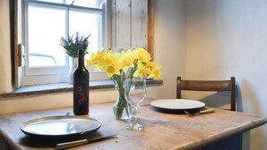 Une table à manger avec une assiette, une bouteille de vin et un vase rempli de fleurs jaunes.