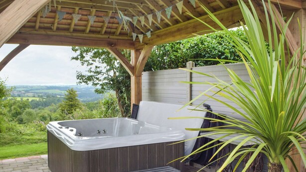 Un bain à remous sous une pergola en bois, avec vue sur la campagne.