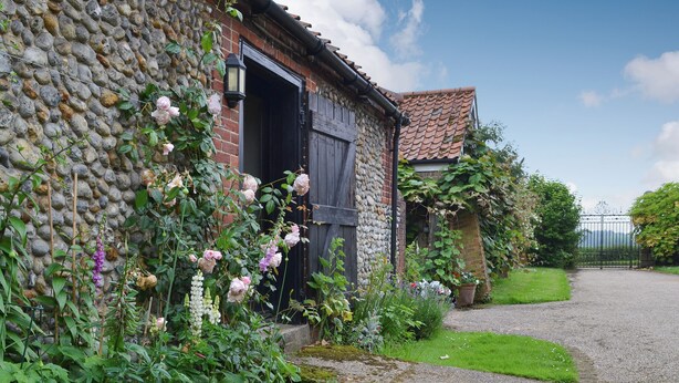 Un edificio de piedra con camino de grava y un jardín con diversas plantas y flores.